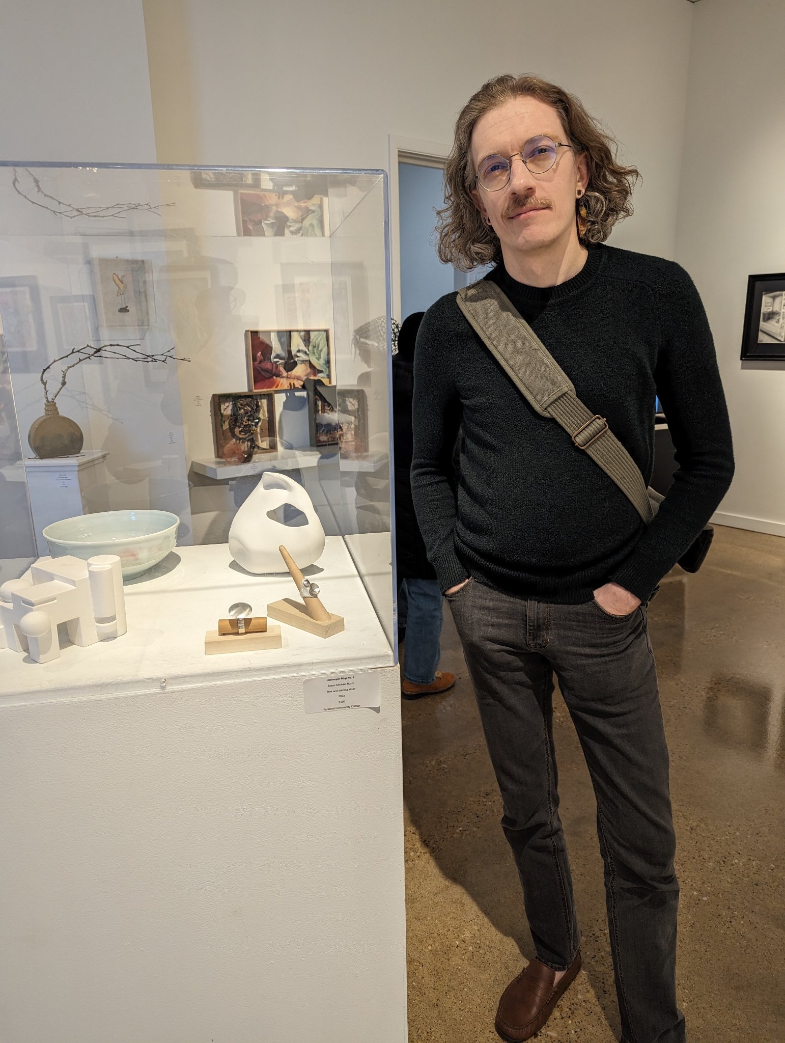 Saxon Burns standing beside his jewelry exhibition case in 2024.